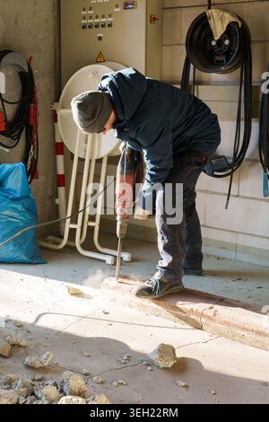 Worker using jackhammer to break concrete floor indoors Stock Photo