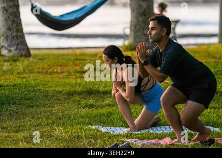 Honolulu, Hawaii, USA - May 19, 2025: A woman and man hold low lunge yoga poses with their palms together during an outdoor class in a Waikiki oceanfr Stock Photo