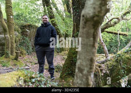 Smiling man wearing hoodie standing in green forest Stock Photo