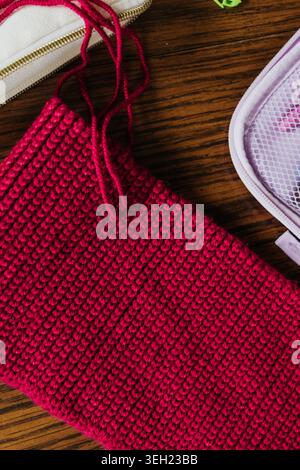 Overhead view of red crochet hat progress surrounded by tools Stock Photo