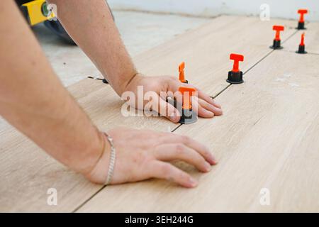 Laying tiles concept with close up worker hand. Tiler, spatula and glue when laying tiles. Pull tabs and wedges for leveling system. Stock Photo