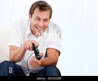 Mid-adult man smiling, leaning forward on couch holding wired controller and showing wedding ring Stock Photo