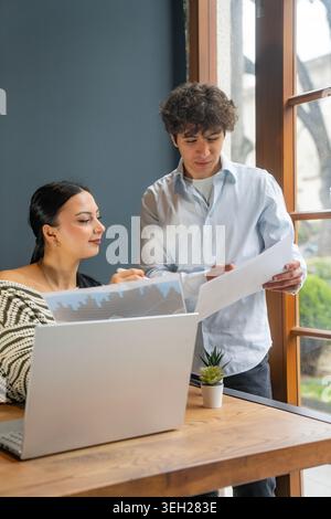 Male and female coworkers reviewing printed business reports and discussing data in a contemporary office. Ideal for corporate teamwork, analytics, fi Stock Photo