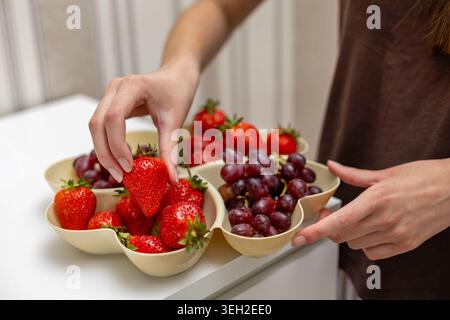 Hand Picking Strawberry From Fresh Fruit Tray. Close-up of hands selecting a ripe strawberry from a divided tray filled with fresh strawberries and Stock Photo