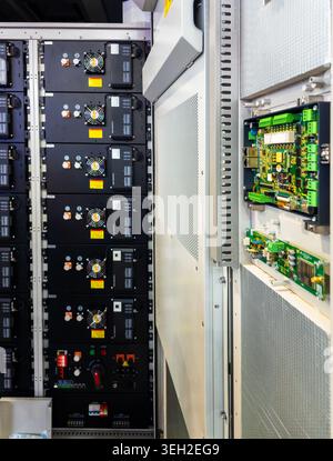 A professional-grade industrial server rack housing modular energy storage units with integrated cooling fans and exposed electronic control boards. Stock Photo