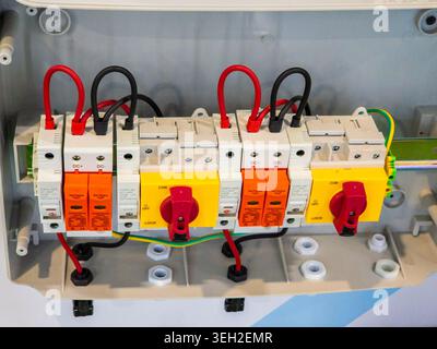 Close-up of a solar power combiner box featuring DC surge protective devices, circuit breakers, and rotary isolator switches with red and black wiring Stock Photo