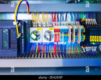 Detailed close-up of a professional electrical control panel featuring a programmable logic controller, illuminated switches, and organized color-code Stock Photo