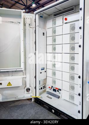 An open white industrial electrical cabinet featuring a modular rack system with battery storage or power distribution components in a factory setting Stock Photo