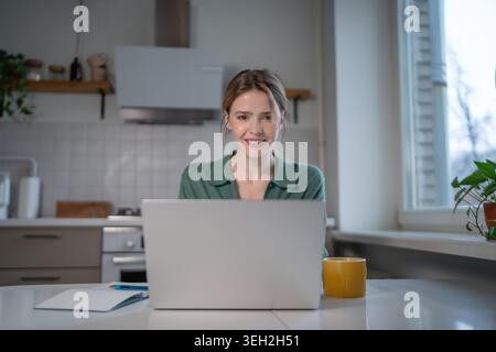 Smiling woman using laptop with satisfaction while remote working at home. Interested female focused looking at computer screen, positive online such Stock Photo