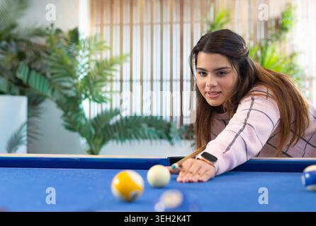Adult woman leaning over blue-felt table in lounge aiming shot with cue stick and cue ball Stock Photo