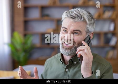 Smiling senior man talking on smartphone, communicating and staying connected using modern mobile technology while relaxing in his comfortable living room Stock Photo