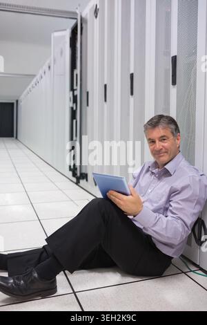 Middle-aged tech sitting on raised floor, using tablet, checking server racks and cable, copy space Stock Photo