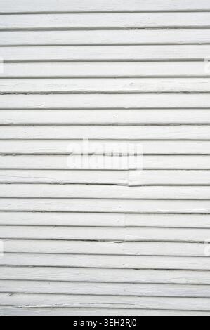 White painted narrow lap wood siding with horizontal slats, visible wood grain, peeling paint, splintered and cracked areas Stock Photo