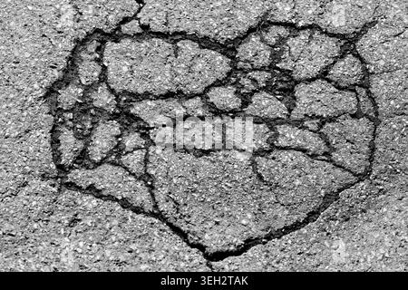 Asphalt Heart. A heart-shaped pattern formed by dark cracks on the surface of a dilapidated and weathered asphalt road in Germany. Black and white. Stock Photo