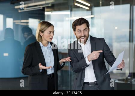 Business colleagues in an office workspace having a heated discussion about a report, showing conflict, misunderstanding, and stress in a professional environment Stock Photo