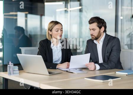 Two diverse business professionals collaborating during a meeting, discussing important documents and working together on a project in a modern office environment Stock Photo