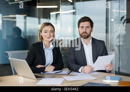 Business partners at an office desk review documents and a laptop during a focused meeting, discussing strategy, planning projects and finalizing a professional agreement Stock Photo