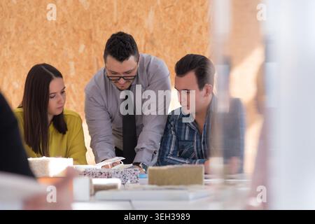 A multi-ethnic group of young architects and engineers, including a woman in a hijab, sit around a table for a collaborative session on material selec Stock Photo