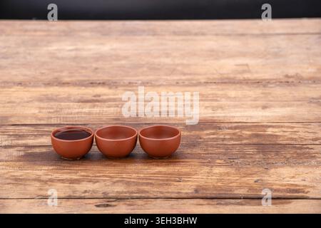 Three handcrafted terracotta clay tea cups sit in a row on an aged rustic wooden table with natural grain patterns visible in the wood surface and the Stock Photo