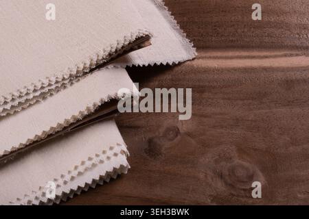 Close-up of stacked natural matka silk fabric samples with raw textured edges displayed on a wooden background. Stock Photo