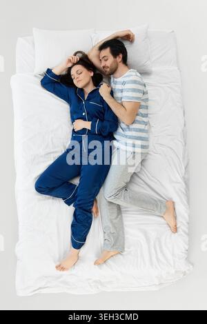 Daughter making funny face while parents laugh on bright white bedding. Stock Photo