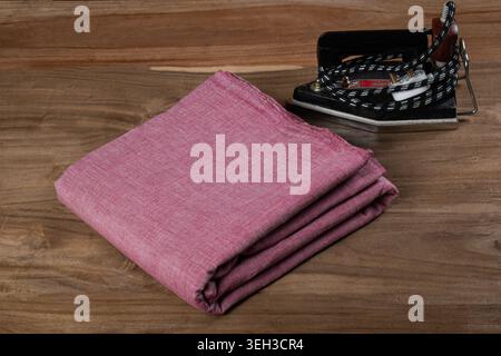 Folded pink cotton chambray fabric with vintage electric iron on wooden background Stock Photo
