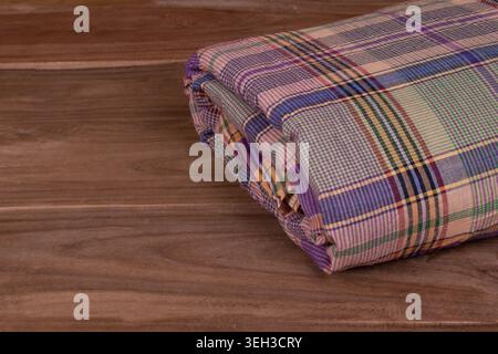 Colorful folded checkered cotton fabric placed on a wooden surface, showcasing woven textile texture and traditional plaid design. Stock Photo