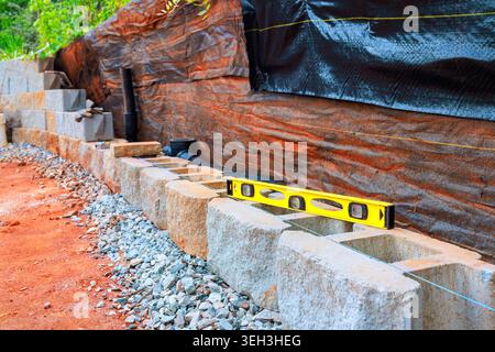 Workers are building retaining stone wall using concrete blocks checking level of structure with tool. Stock Photo
