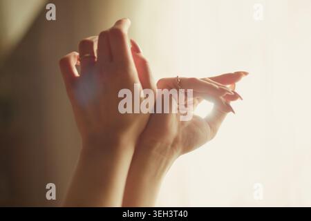 Close up of young adult womans hands stretching fingers in sunlight, expressing self care and mindfulness. Suitable for wellness campaigns, beauty branding, close up Stock Photo