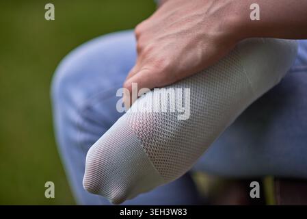 Close-up of a person holding a foot in a torn gray sock, outdoors, showing wear and a hole near the toes; concept of clothing damage, discomfort, and Stock Photo