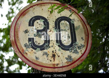 Vintage rusty speed limit 30 sign, heavily weathered and partially covered in green lichen and moss. Stock Photo