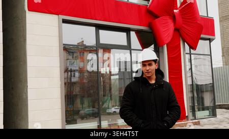 Man in a white hard hat standing near a building entrance Stock Photo