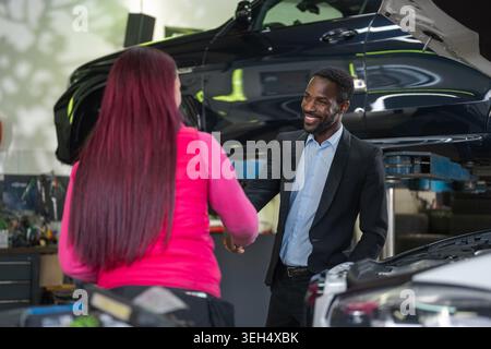 Female mechanic completing the car service, shaking hands and returning the keys to a satisfied, smiling client, a successful businessman. Stock Photo