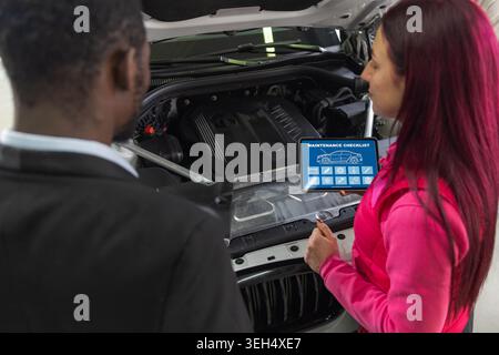 Female mechanic talking with a client in a car service, using digital tablet for diagnostics, a modern approach to vehicle maintenance. Stock Photo