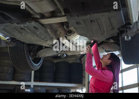 A female mechanic inspects and repairs a vehicle in a modern garage, using tools for maintenance and service. Stock Photo