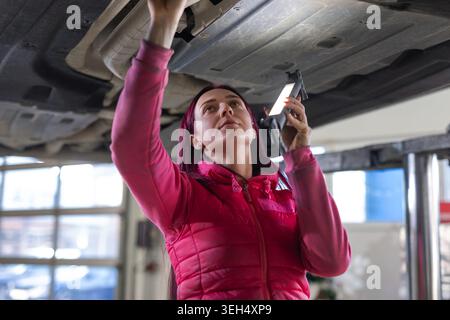 A female auto technician inspects and repairs a vehicle in a garage using tools and diagnostic equipment for maintenance. Stock Photo