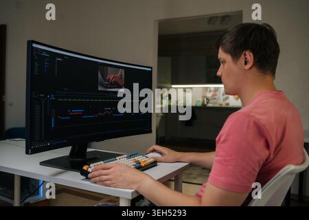 Filmmaker male working on video editing with specialized software on large curved monitor, focusing on post-production tasks in home office Stock Photo