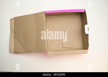 Empty open brown cardboard box lying flat on a plain surface, top view of generic packaging, shipping and storage container material. Stock Photo