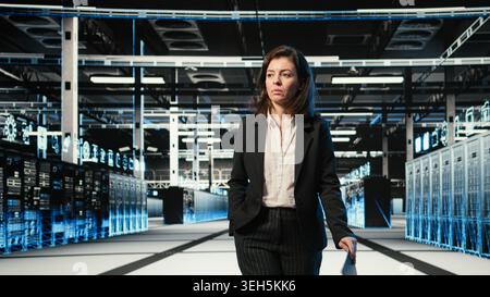 Data center manager inspecting blue wireframe mesh hardware rackmounts. System administrator walking through server hub rows, looking at AR digital twin data streams Stock Photo
