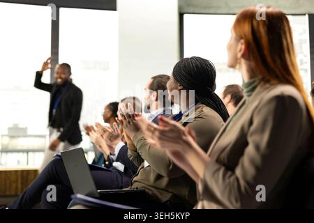 Audience clapping hands and greeting public speaker at business conference, applauding and paying attention to discussion. Diverse group of professionals attend corporate event. Stock Photo