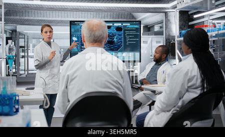 Medical school professor mentoring researchers about molecular biology concepts. Woman in laboratory using display to explain DNA organism structure to students, camera B Stock Photo