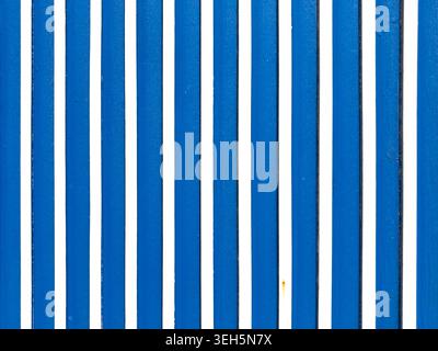 A close-up shot features a pattern of bright blue painted wooden slats separated by crisp white gaps, creating a clean geometric minimalist backdrop w Stock Photo