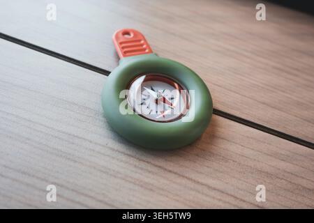Portable green and orange compass on a wooden table, suitable for travel use and practical field tasks.  Stock Photo