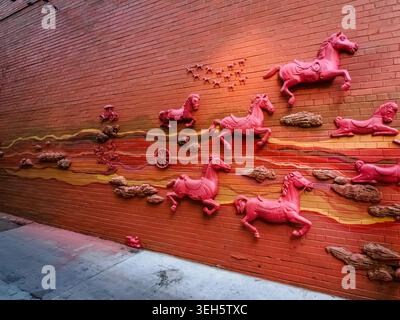 Red bas relief mural of horses on an orange brick wall at 16th Street in Denver, Colorado Stock Photo