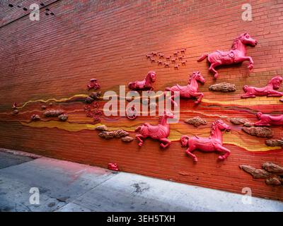 Red bas relief mural of horses on an orange brick wall at 16th Street in Denver, Colorado Stock Photo