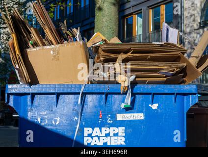 Blue waste paper recycling container filled with flattened cardboard boxes and packaging material on a city street in Berlin, Germany. Stock Photo