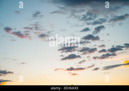 Sky showing soft pink and gray clouds scattered across a peaceful gradient of blue to orange hues, capturing the serene beauty of a sunset or dusk mom Stock Photo