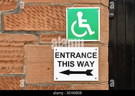 Accessible entrance sign with wheelchair symbol and directional arrow mounted on a brick wall, representing disability access, inclusion and public ac Stock Photo