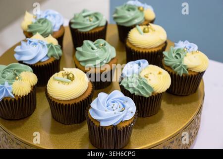 Assorted cupcakes decorated with pastel blue, green, and yellow buttercream frosting on a gold stand, perfect for celebrations, parties, and dessert d Stock Photo