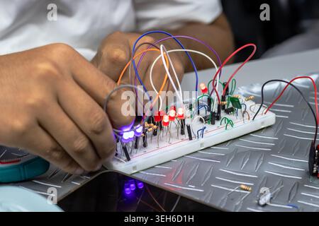 Close-up of hands assembling and testing an electronic circuit on a breadboard with glowing LEDs, jumper wires, and components in a workshop or electr Stock Photo